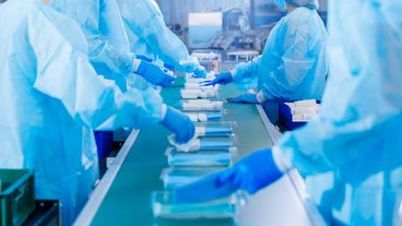 Produktionslinie im Reinraum mit Mitarbeitenden in Schutzkleidung beim Verpacken von Hygieneartikeln