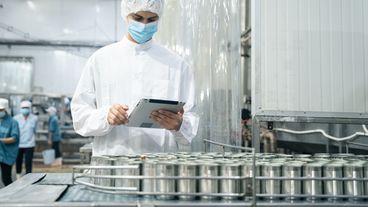 Mitarbeiter mit Schutzkleidung bei der Qualitätskontrolle in der Lebensmittelproduktion mit Tablet