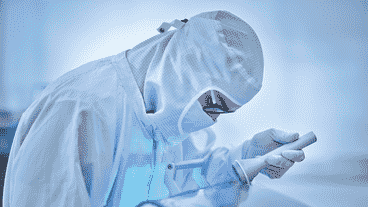 Fachkraft in Reinraumbekleidung inspiziert glatte Oberfläche mit Handlupe unter kontrollierten Bedingungen